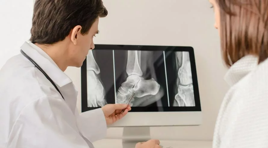 Arztbesuch wegen Gelenkschmerzen: Arzt zeigt Patientin Röntgen-Aufnahmen am Computer
